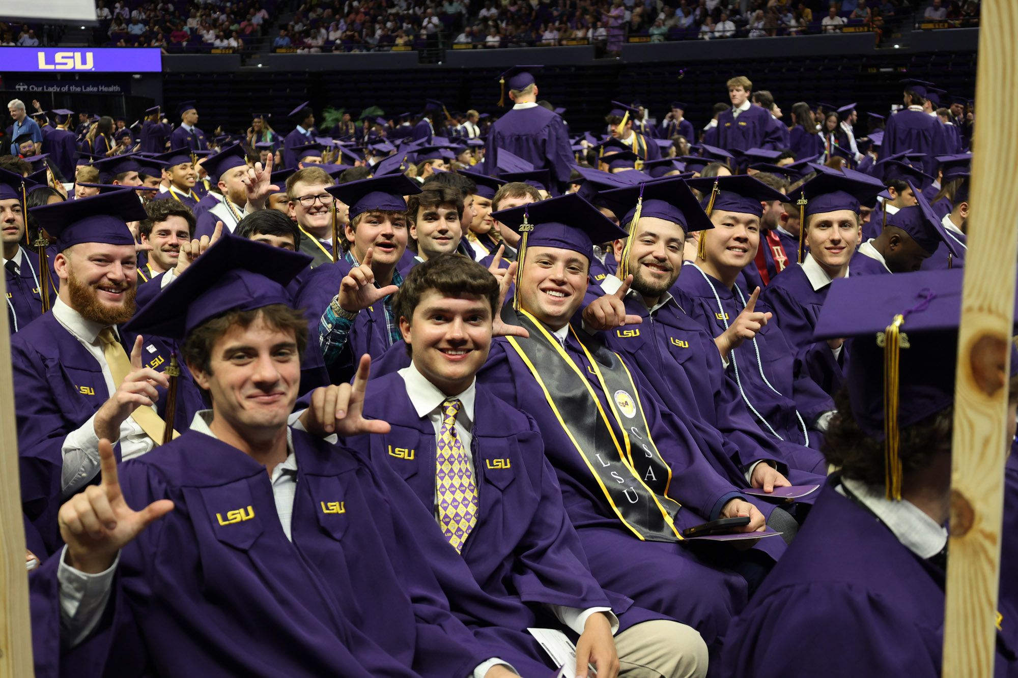 LSU graduates sit at commencement and give the L sign