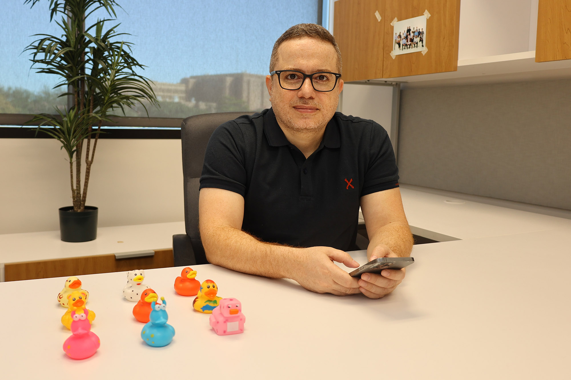 Nash Mahmoud in his office at his desk with a phone and 9 rubber ducks