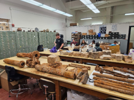 Students processing the archaeological finds from the Old LSU Site. In the foreground are architectural artifacts such as iron columns, braces, and window weights; in the background are large fragments of marble stonework.