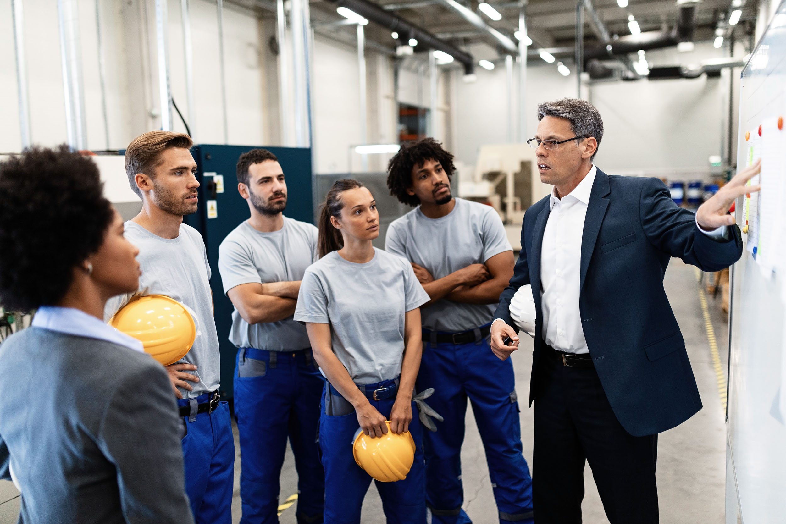 man in suit talking to workers in coveralls and hard hats