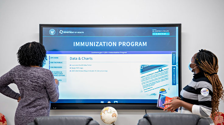 Students look at immunization reports on a large touchscreen television