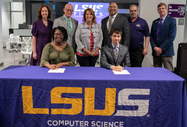 LSUS students Eliana Gafford and Joseph Barnes at table draped with LSUS Computer Science cloth sign fellowship papers as group stands behind them