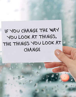 Photo of a hand holding a white sheet of paper with the words "If you change the way you look at things, the things you look at change."