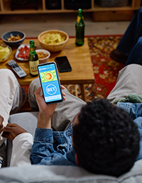 Young adult using a sports betting app while watching sports with friends.