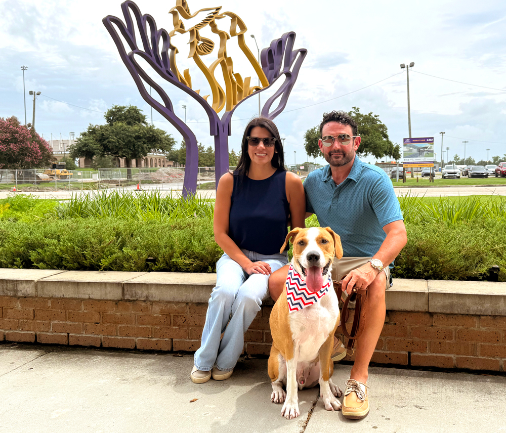 Dawn Amato and Adam Cutrer with Dumpster in front of LSU Vet Med with Helping Hands sculpture in the background